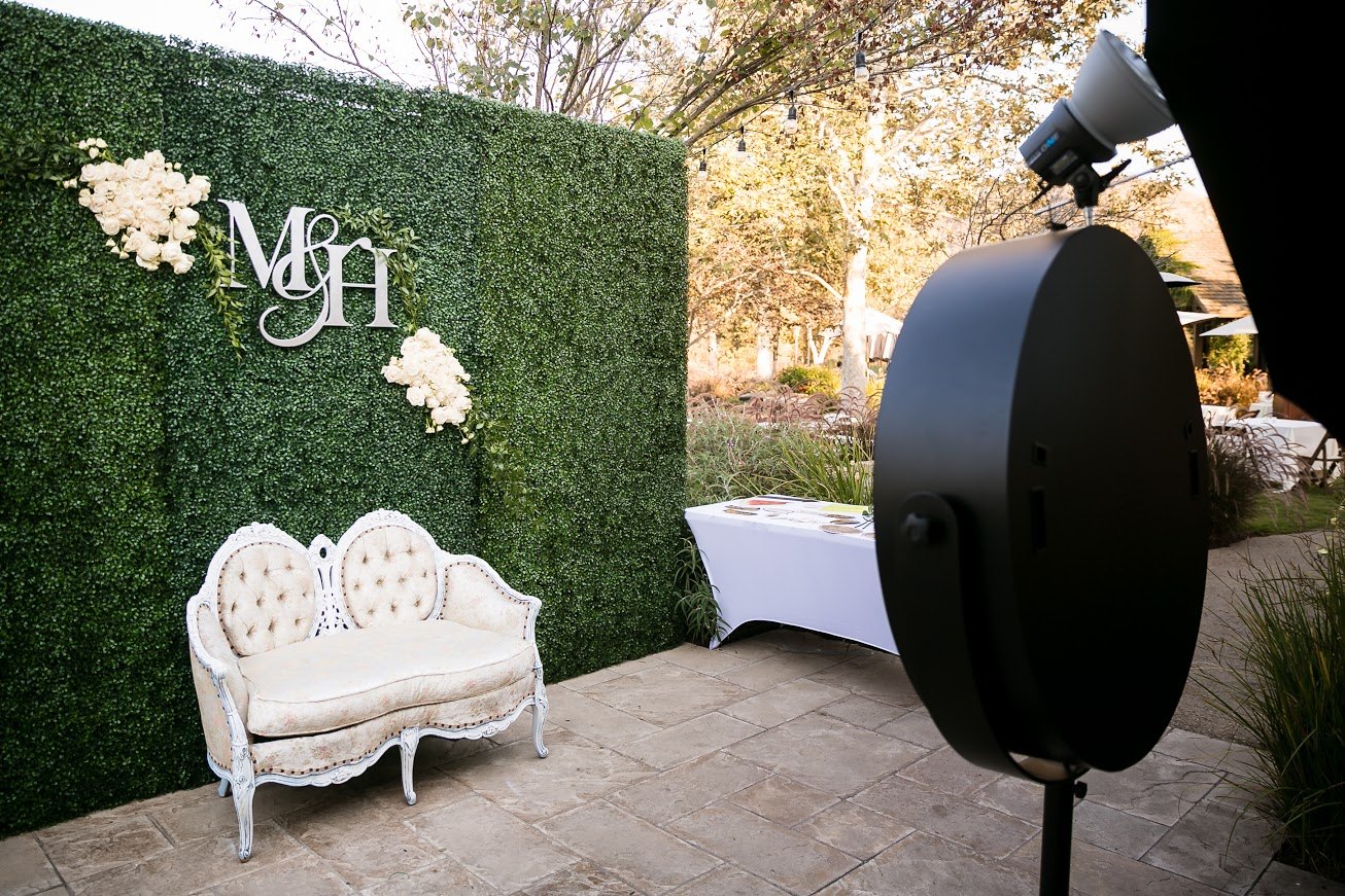 The booth facing an M&H monogram greenery wall with a white vintage loveseat