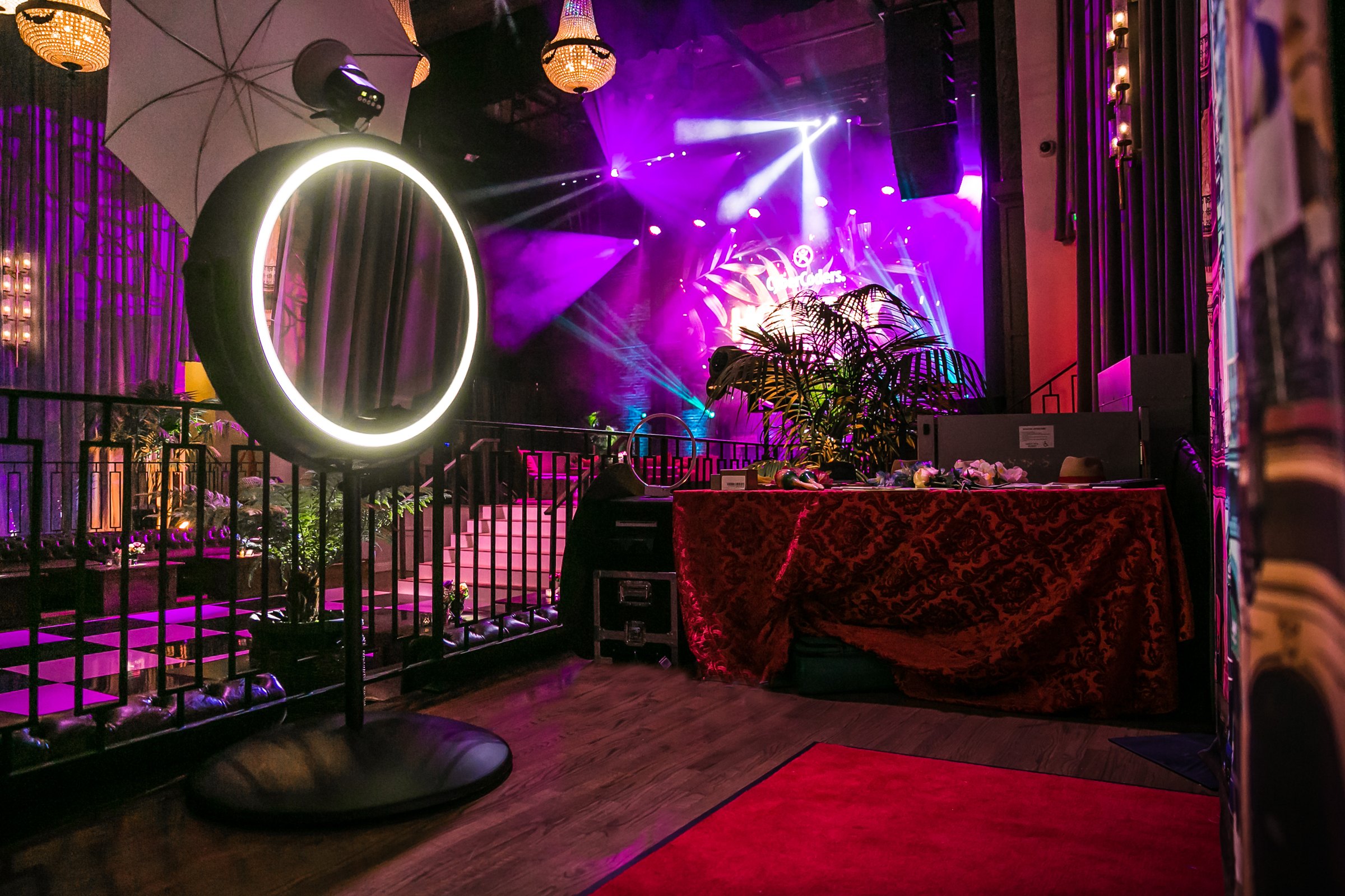 The mirror booth glowing on a balcony in a purple-lit venue, red carpet in front