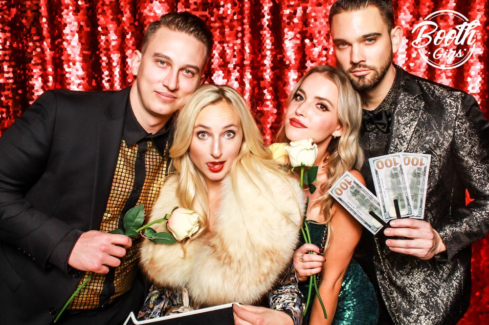 Four guests in fur and sequins with prop money on the red sequin wall