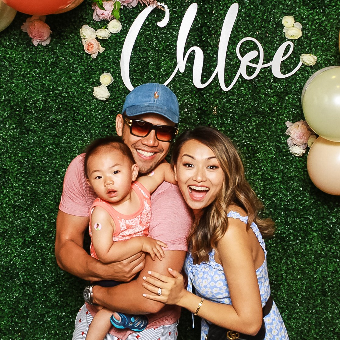 A family laughing in front of the Chloe greenery wall at a baby shower