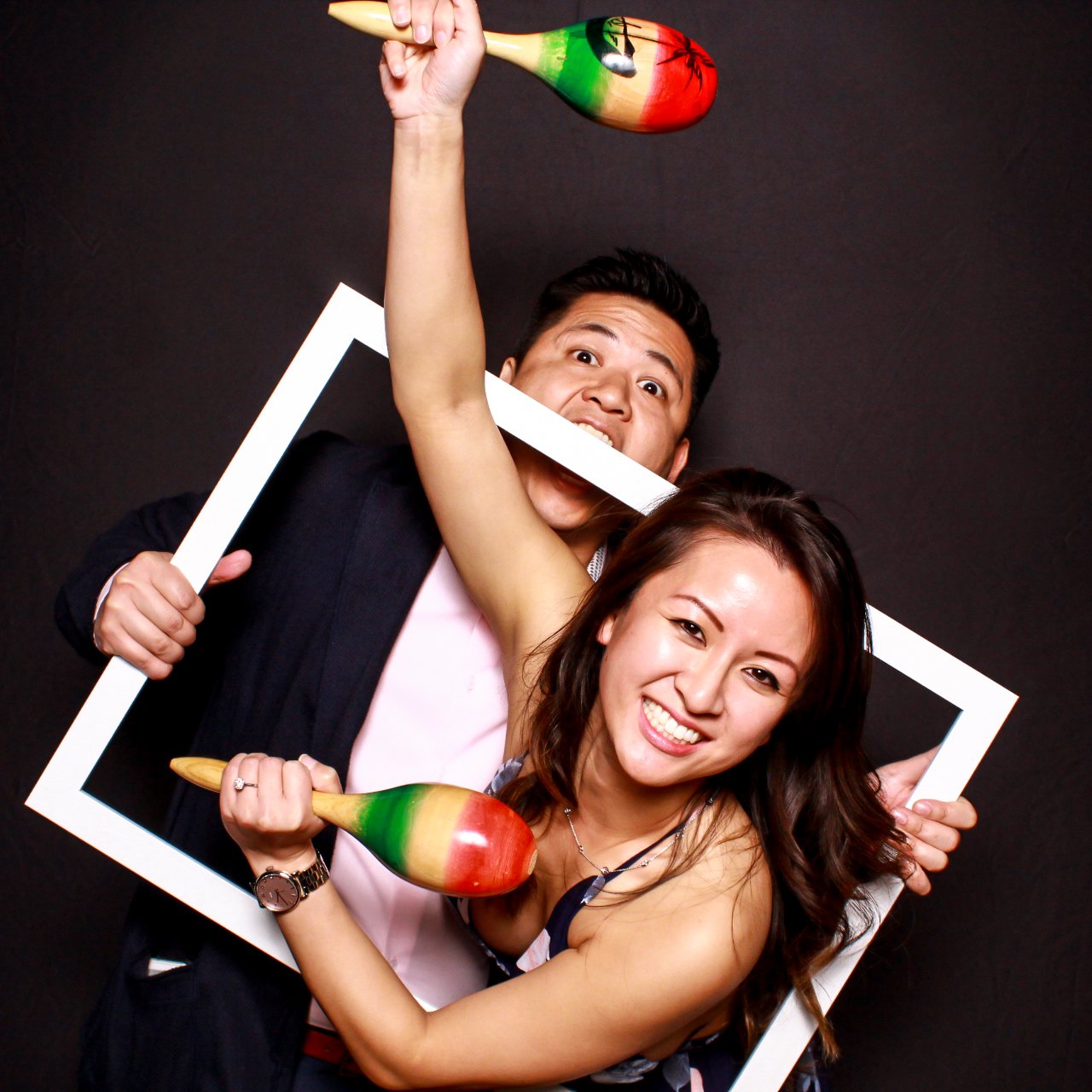 A couple jumping into a white frame prop on a black backdrop