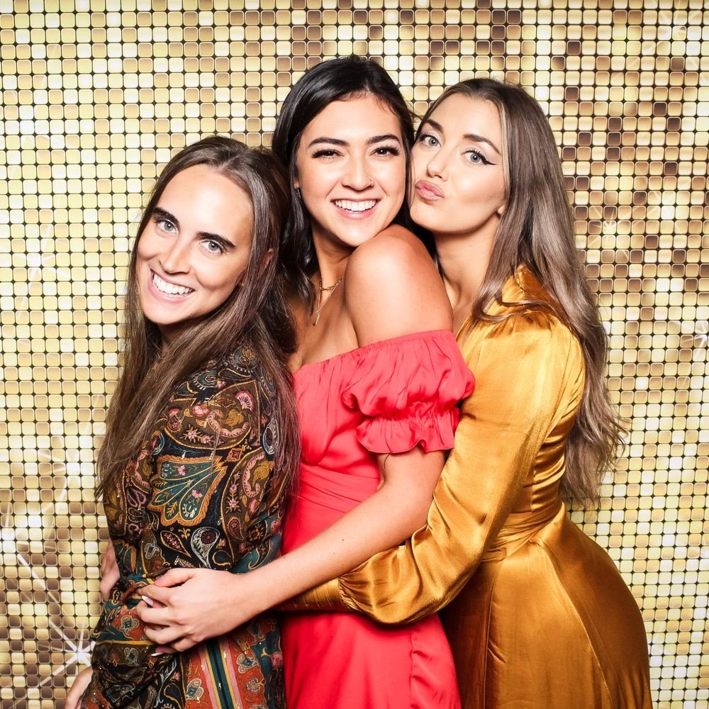 Three friends in bright dresses on the gold sequin wall