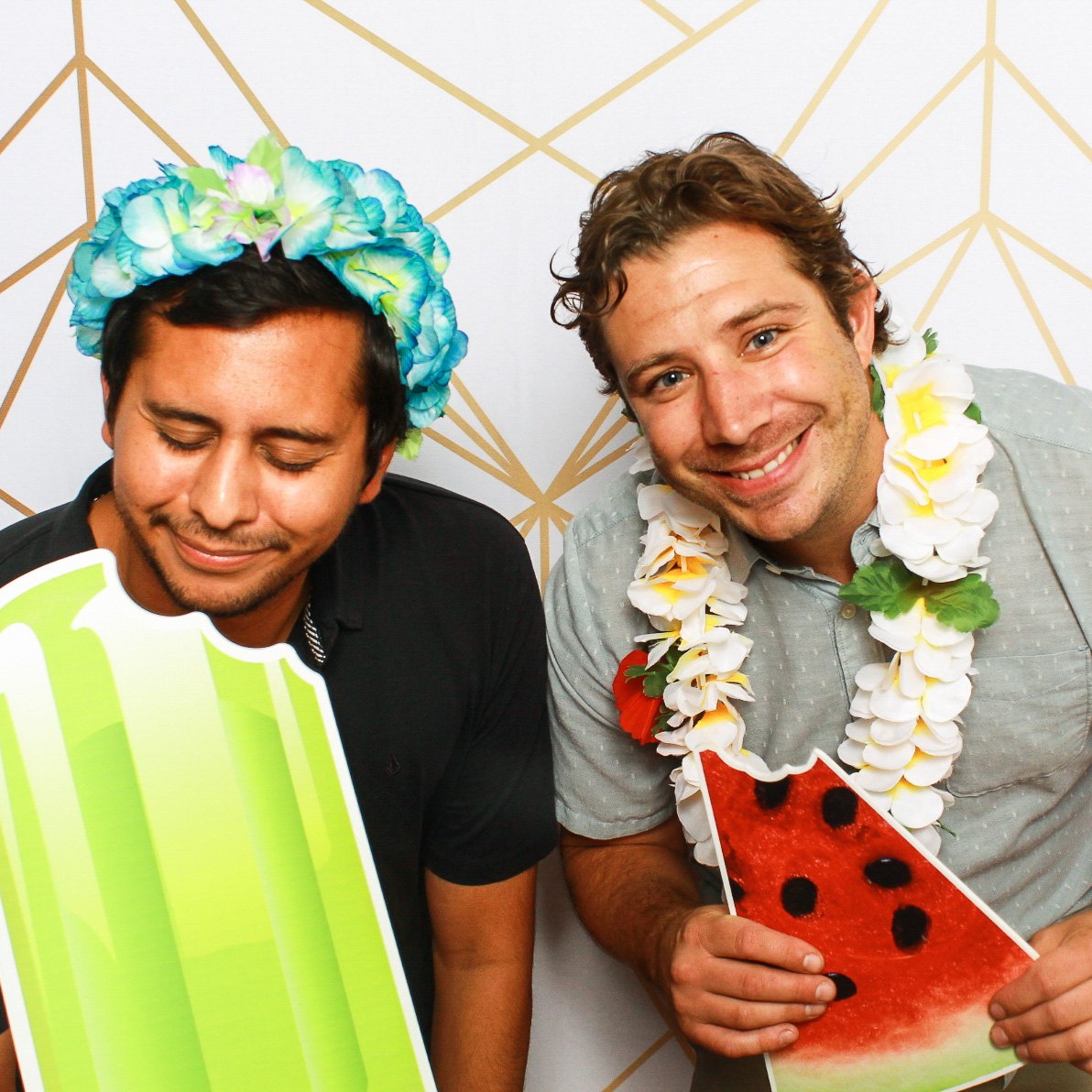 Two guests with a watermelon prop and a flower crown on a gold-line backdrop
