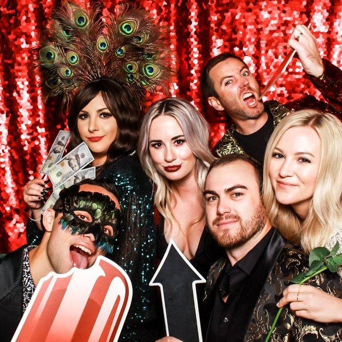 A party group with a peacock headpiece and props on the red sequin wall