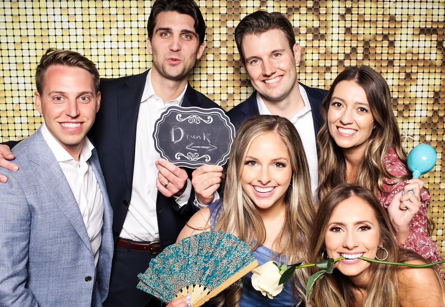 Wedding guests with a monogram sign, fans and roses on the gold sequin wall