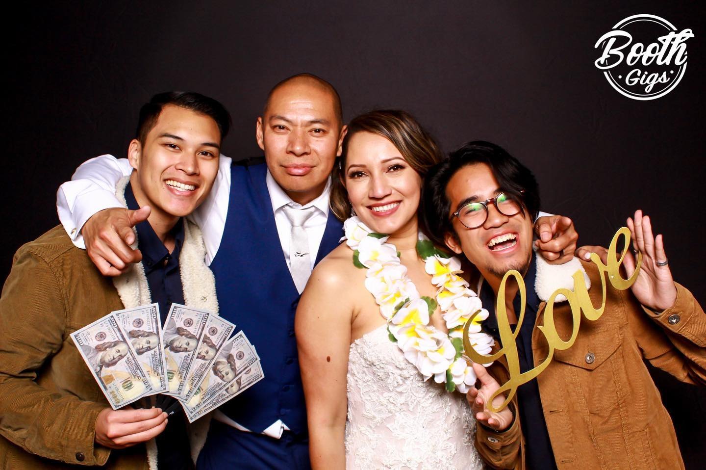 Newlyweds and friends with a gold Love sign and money props on black